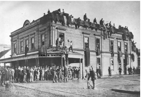 The Alexander Turnbull Library note that this photographs shows Te Aro House after the fire of 18 April 1885 but it is in fact a record of the earlier 1879 Opera House fire. Photographer James Bragge (1833 – 1908) staged a re-enactment of the … “James Smith Limited during the Imperial Opera House fire. Staff are hanging blankets out of windows [presumably these are wet blankets to protect the building from the fires nearby] and in the foreground a fireman is connecting a hose to the mains supply.” Te Papa webpage accessed June 2012. http://collections.tepapa.govt.nz/objectdetails.aspx?oid=127501      James Smith Ltd, Te Aro House after the fire. James Smith Ltd :Photographs of personnel, activities and shops. Ref: PAColl-3332-1-3. Alexander Turnbull Library, Wellington, New Zealand. http://natlib.govt.nz/records/23084720 